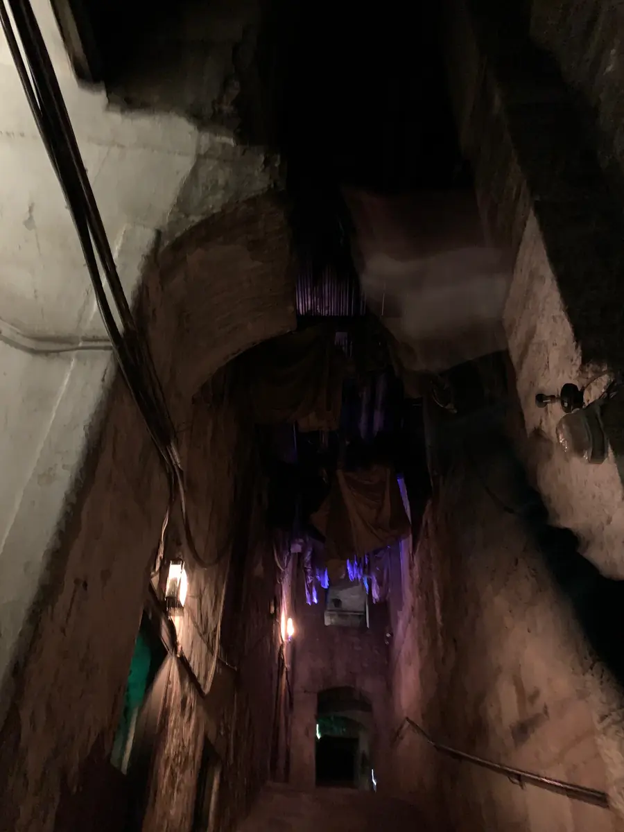 A dim, steep lane underground at Mary King's Close, stone walls rising on both sides and a faint light at the far end