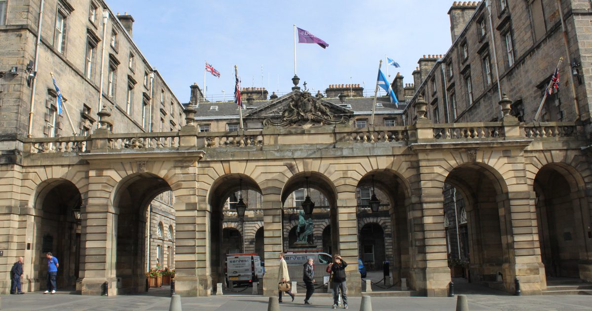 The arcaded screen of Edinburgh's City Chambers on the Royal Mile, seven stone arches under a balustrade and flags, with the courtyard behind